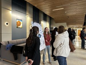A student stands at their research poster and shares information with viewers