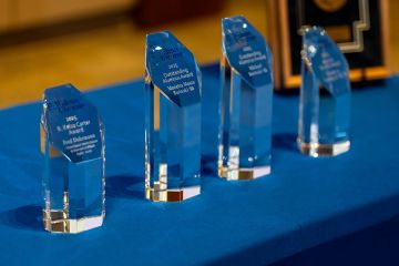 Five alumni awards sitting on a table with a blue tablecloth