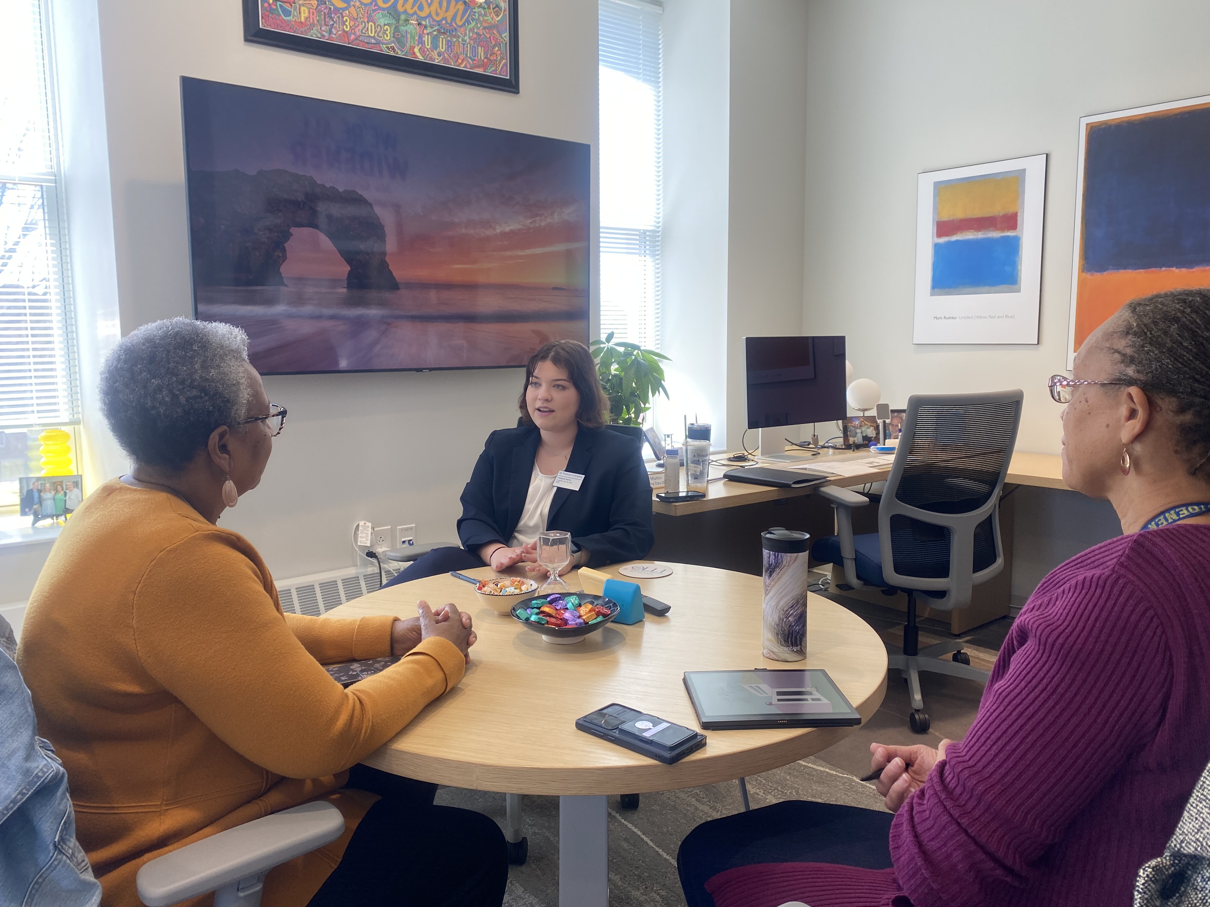 Lizzy sits a round table for a meeting with two women.