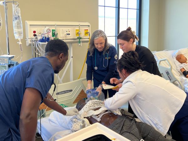 President Robertson squeezes an oxygen bag on a mannequin alongside nursing students during a nursing simulation exercise.