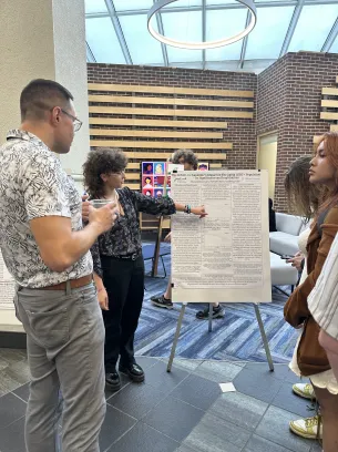 A student points to their poster presentation while other students look and listen