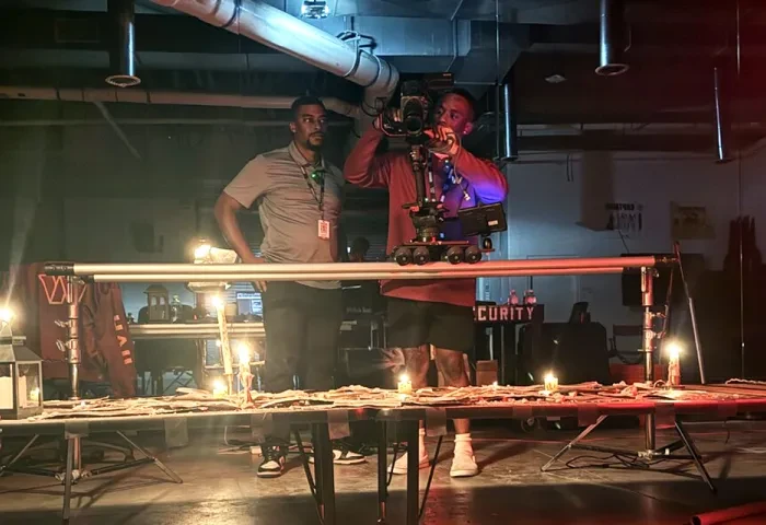 Two men work behind the scenes on a film production, with one holding a camera
