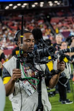 Dakarai Daniel holds a camera on the sidelines of a football game