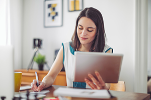 Adult student at home taking notes in meeting on iPad/tablet