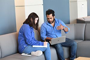Faculty member sitting on cough with student explaining mathematics problem to a student