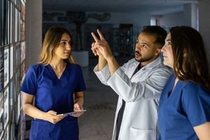 A male doctor shows two women medical students a series of X-ray scans on a wall.