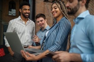 One woman and three men in business attire are smiling and reading a laptop.