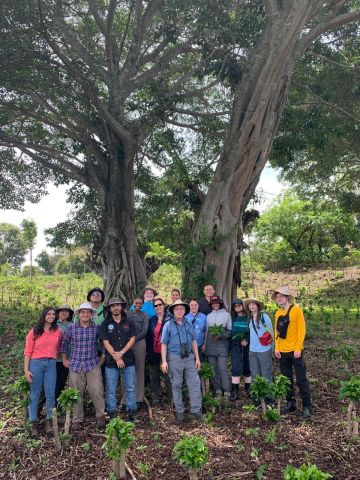 A group of Widener students, faculty, and others stand beneath a large tree, smiling.