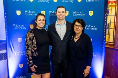 Three members of Fred Dohrmann's family stand in front of a blue Widener backdrop