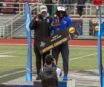 Matayo McGraw stands on the podium with his coach and holds a national champion triple jump sign
