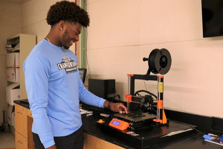 Student stands at a 3D printer in a mechanical engineering lab
