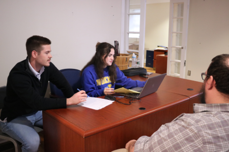 tax clinic story 960x640 Students sit across from a client at a dark wooden desk. There are papers and a laptop on the desk