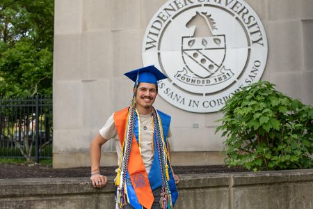Leo-Paul Wahl poses on campus in his graduation cap and his regalia cords.