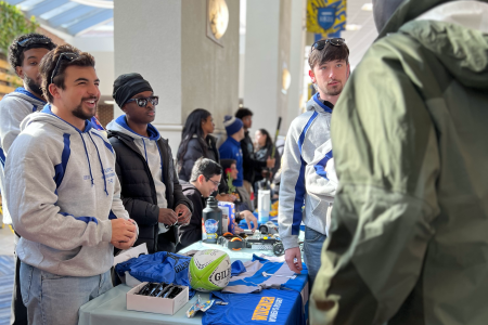 Four members of the men's rugby team stand around a table speaking to a prospective member