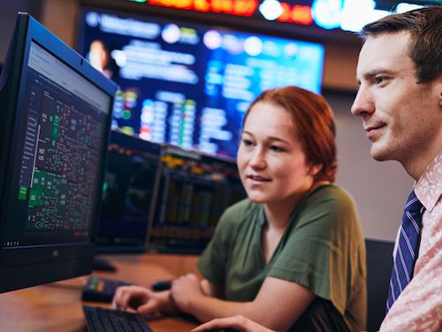 students work together in finance lab with stock ticker in background