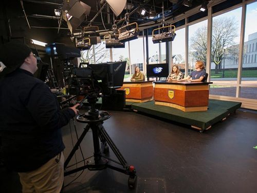 A camera operator films students at a news desk in Widener's WUTV studio.
