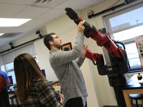 A male student examines a robotic arm in Widener's robotics lab.