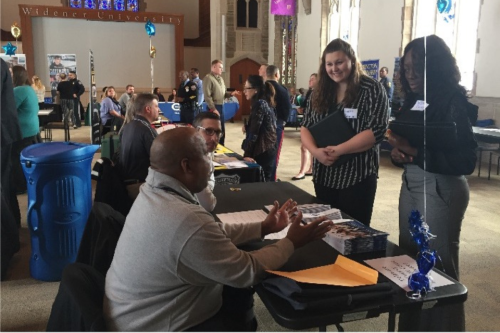 cj career fair event 960x640 Two students in professinal attire approach a table and talk to a prospective employer